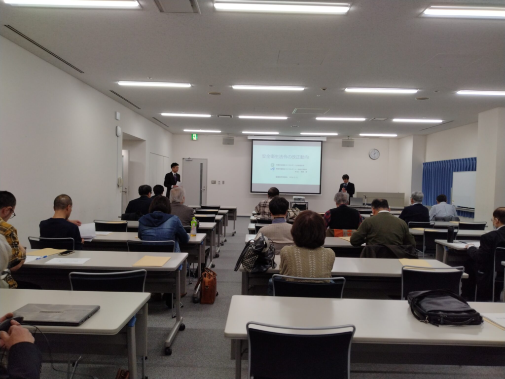 明るい会議室で、講師の解説を真剣に聴講する白衣やスーツ姿の医師たちの様子。